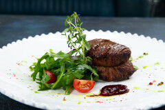 tagAlt.Beef medallions with arugula and tomatoes in a plate. Against a dark background