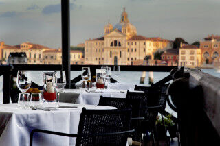 tagAlt.Empty restaurant tables with vine glasses, overlooking the San Giorgio Maggiore church in Venice.