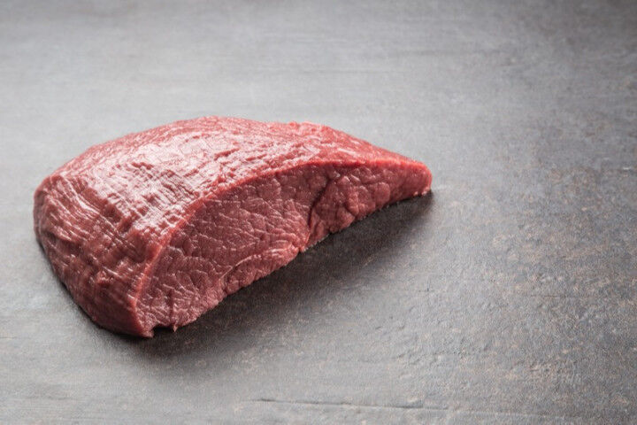 Portion of raw beef thigh on dark butcher board